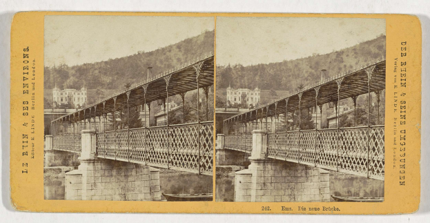 Schwarz-weiß-Fotografie einer alten Brücke, die einen Fluss in Leipzig, Deutschland, überspannt, mit Gebäuden, Bäumen und einem Hügel im Hintergrund.