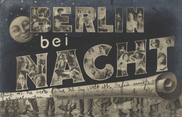 Schwarz-weiß-Foto einer Gruppe von Menschen, die vor einem Schild mit der Aufschrift "Berlin Bei Nacht" lachen und strahlen, im Hintergrund ein Mond, das Schild mit Sternen und Streifen geschmückt.