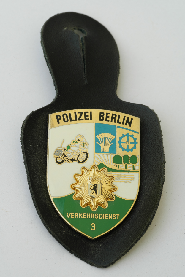 Ein Polizeistern mit der Aufschrift "Polizei Berlin", der ein blaues Schild mit einem weißen Stern in der Mitte und einen weißen Rand hat, auf einer Oberfläche.