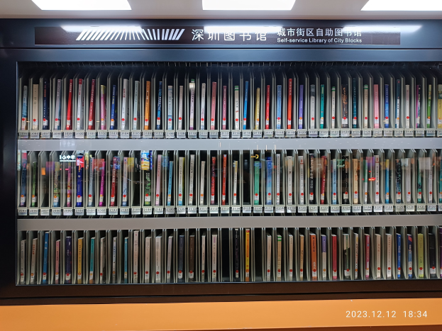 Eine gut beleuchtete Bibliothek mit Bücherregalen in Reihen, ein Textbrett und ein Wasserzeichen unten, das an eine Selbstbedienungsbibliothek von Stadtblöcken erinnert.