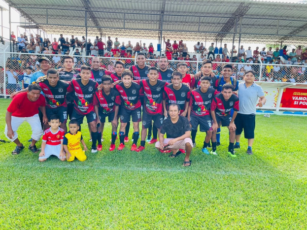 Gruppe von Männern auf einem Fußballfeld mit einem Siegesschild "Fotos Ugarte U-17 vs U-18" unter einem bewölkten Himmel.