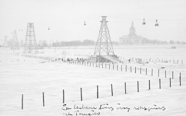 Schwarze und weiße Fotografie eines Skilifts in einem verschneiten Feld mit Stützpfählen, Überseilbahn, Bäumen und einem Gebäude im Hintergrund, mit Text am unteren Rand.