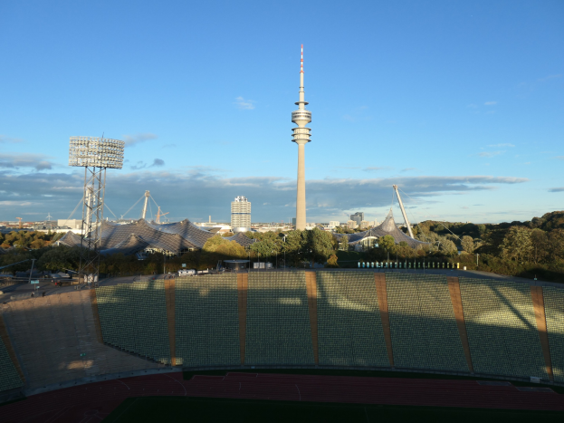 Olympiastadion in Berlin, Deutschland, mit dem Fernsehturm im Hintergrund, umgeben von Bäumen, Gebäuden und Lichtern unter einem bewölkten Himmel.