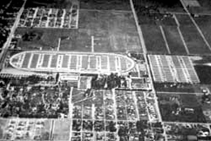 Schwarzer und weißer Luftaufnahme eines Fussballfeldes in städtischer Umgebung, umgeben von Gebäuden, Bäumen und Fahrzeugen.