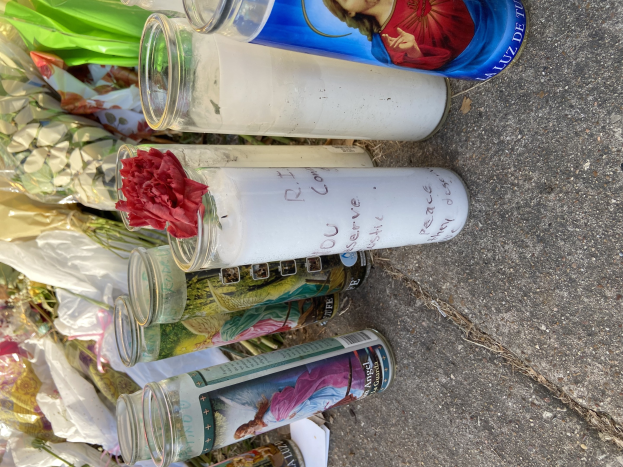Provisorisches Straßenranddenkmal mit Glasflaschen mit Fotos und Text, einem Blumenstrauß und angezündeten Kerzen.