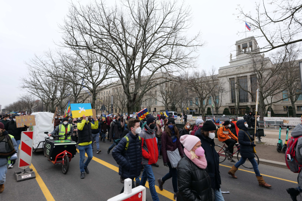 Eine große Gruppe von Menschen nimmt an einer Protestdemo in Washington, D.C. am 21. Januar 2020 teil und marschiert eine Straße entlang mit Schildern, Bannern und Fahrrädern vor einem Gebäude mit Bäumen und Schildern unter einem klaren blauen Himmel.