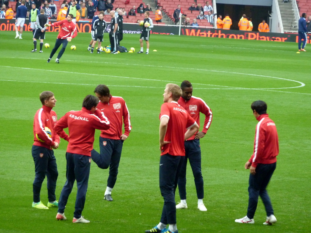Eine Gruppe von Spielern auf einem grünen Feld mit Fußballen und einer Zuschauermenge im Hintergrund.