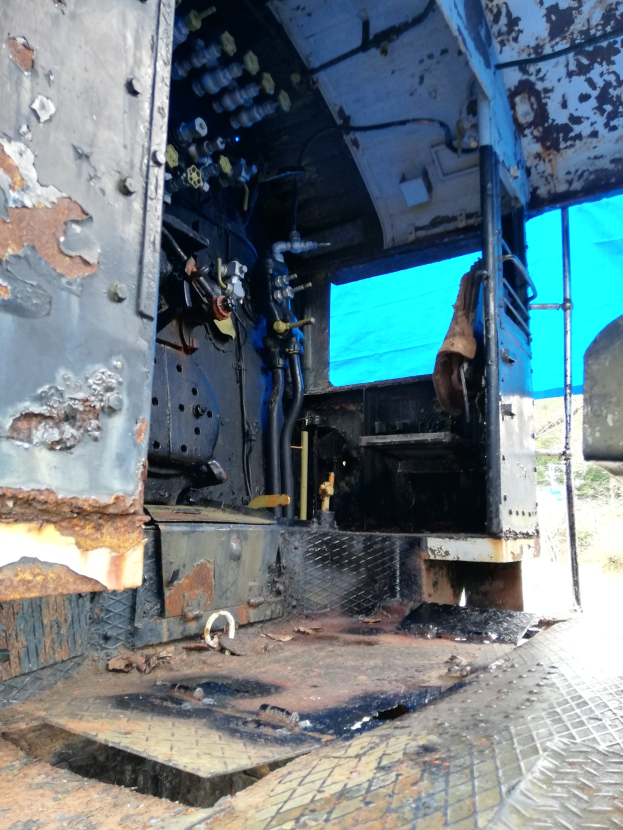 Das Innere eines verrosteten, baufälligen Lastwagens mit sichtbaren Gebrauchsspuren, vor dem Hintergrund von Bäumen und einem klaren blauen Himmel.