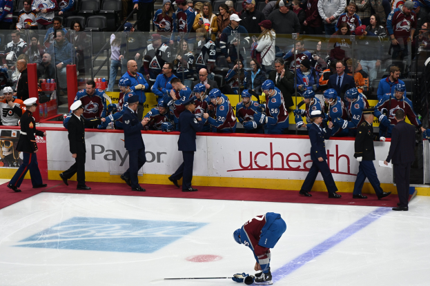 Eishockeyspieler auf dem Eis umgeben von Teamkollegen und Gegnern, mit Zuschauern im Hintergrund und Arena-Böden, die "Colorado Avalanche vs San Jose Sharks - 3/24/15 NHL Pick, Odds, and Prediction" anzeigen.