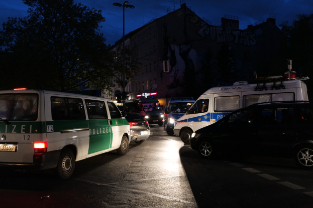Eine Gruppe von Polizeiwagen, darunter ein Van, ein Auto und ein Rad, geparkt am Straßenrand bei Nacht mit Gebäuden, Bäumen, Laternenpfählen und einem sternenklaren Himmel im Hintergrund.