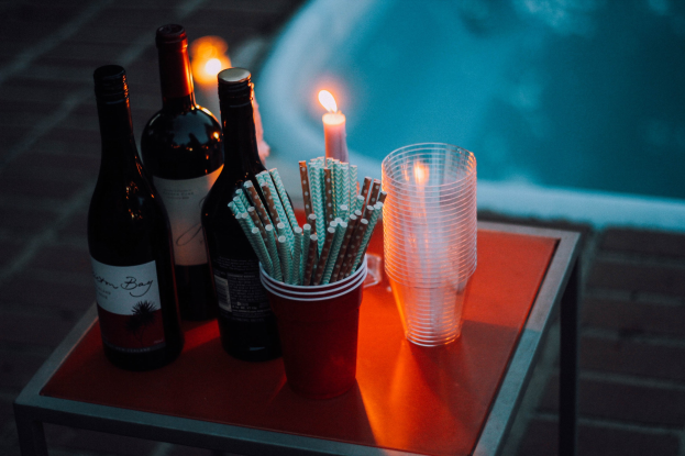 Ein Tisch am Swimmingpool mit zwei Weinflaschen, einer Kerze, Gläsern und Strohhalmen vermittelt eine entspannte Abendstimmung.