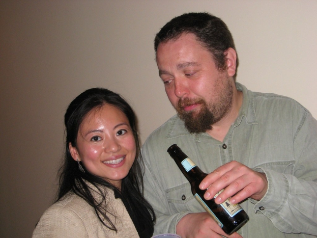 Ein Mann mit einer Flasche schaut eine lächelnde Frau an einer Wand im Hintergrund an.