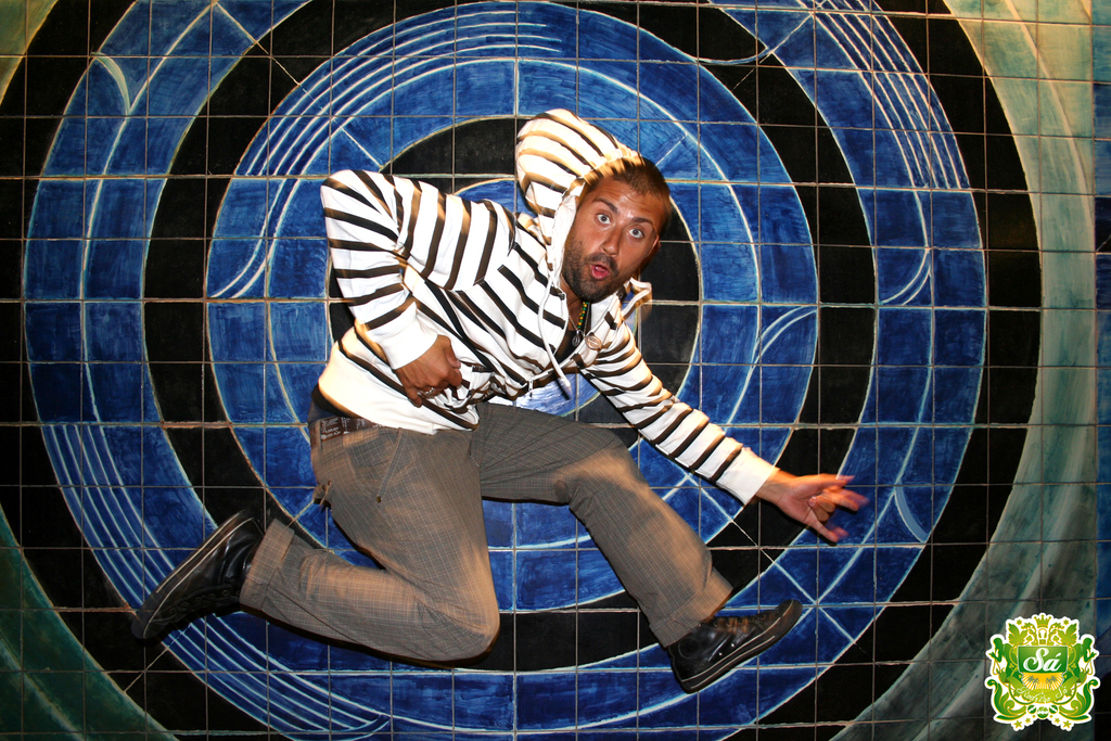 Ein Mann tanzt vor einem bunten Hintergrund mit einem Logo in der rechten oberen Ecke.