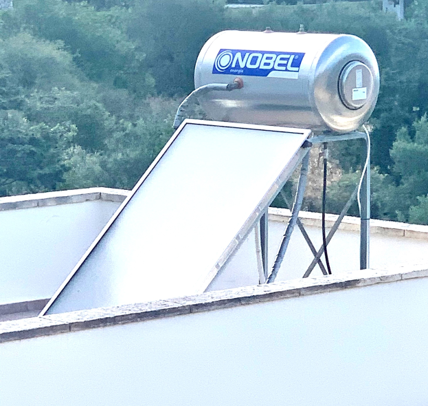 Solarwassererwärmer mit Speicher auf einem Gebäude Dach montiert, Bäume im Hintergrund sichtbar.