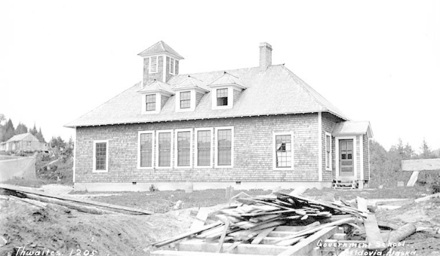 Schwarz-weiß-Foto eines Regierungsgebäudes aus dem Jahr 1905 mit Fenstern, Türen, umgeben von Bäumen und einem klaren Himmel und hölzernen Brettern unten mit der Aufschrift "Regierungsgebäude, Thwaites, 1905".
