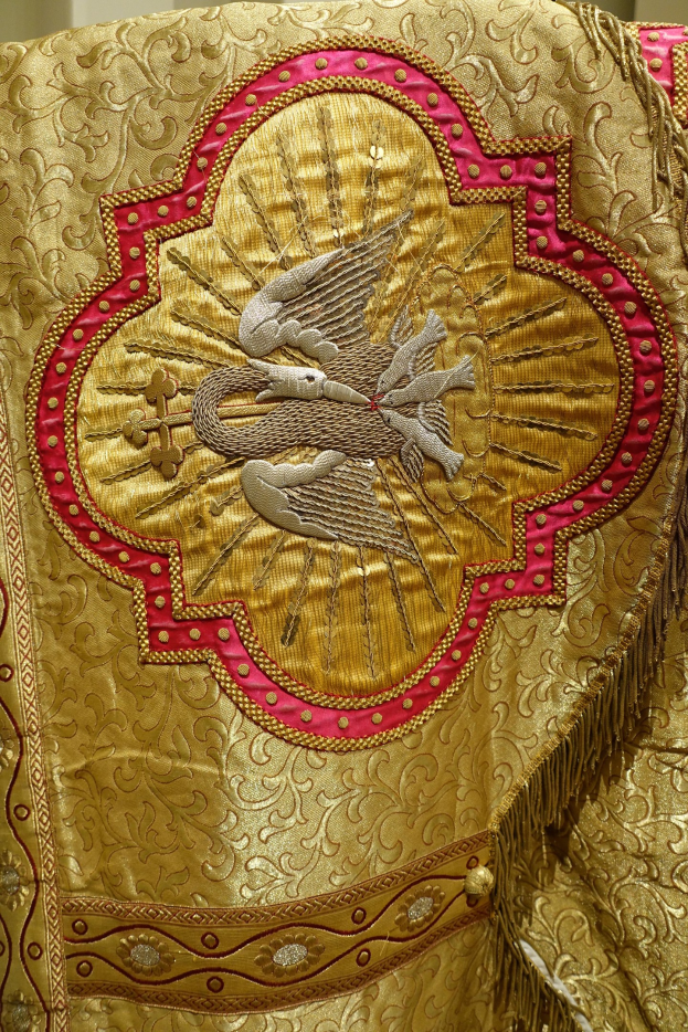 Nahaufnahme eines Priestergewandes mit aufwendiger goldener und roter Stickerei an einer Wand im Hintergrund