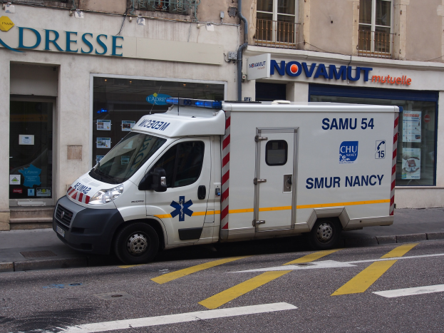 Ambulanz auf der Straßenseite vor einem Gebäude mit Krankenhausschild und verschiedenen Anschlägen geparkt.