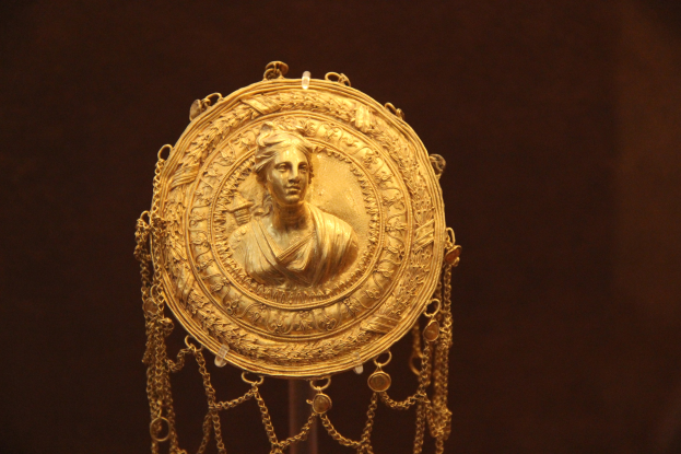 Goldene Medaille mit einer Frauengestalt, verziert mit feinen Details und einem luxuriösen Design, vor einem dunklen Hintergrund.