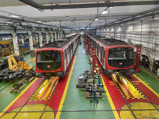 Zwei Züge auf Schienen innerhalb eines großen Industriegebäudes mit Maschinen und Equipment, das eine Wand mit Rohren und Deckenbeleuchtung auf der rechten Seite zeigt, Teil der Daimler Group's Einrichtung.