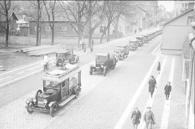 Ein Schwarz-Weiß-Foto einer belebten Straße in Berlin aus den 1930er-1940er Jahren, das Autos, Passanten, Gebäude mit Fenstern, Bäume und einen klaren Himmel zeigt, mit Text am unteren Rand, der '1930er-1940er Jahre deutsche Autos in Berlin' lautet.