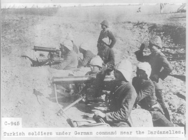 Schwarz-weiß-Fotografie von türkischen Soldaten unter deutschem Kommando in der Nähe der Dardanellen, die Helme tragen und Waffen halten, mit Text unten.