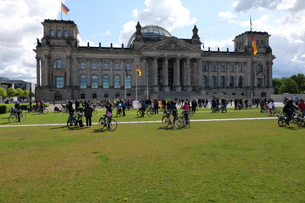 Gruppe von Menschen, die vor dem Reichstaggebäude in Berlin, Deutschland Fahrrad fahren, mit Bäumen, Pflanzen und einem bewölkten Himmel.