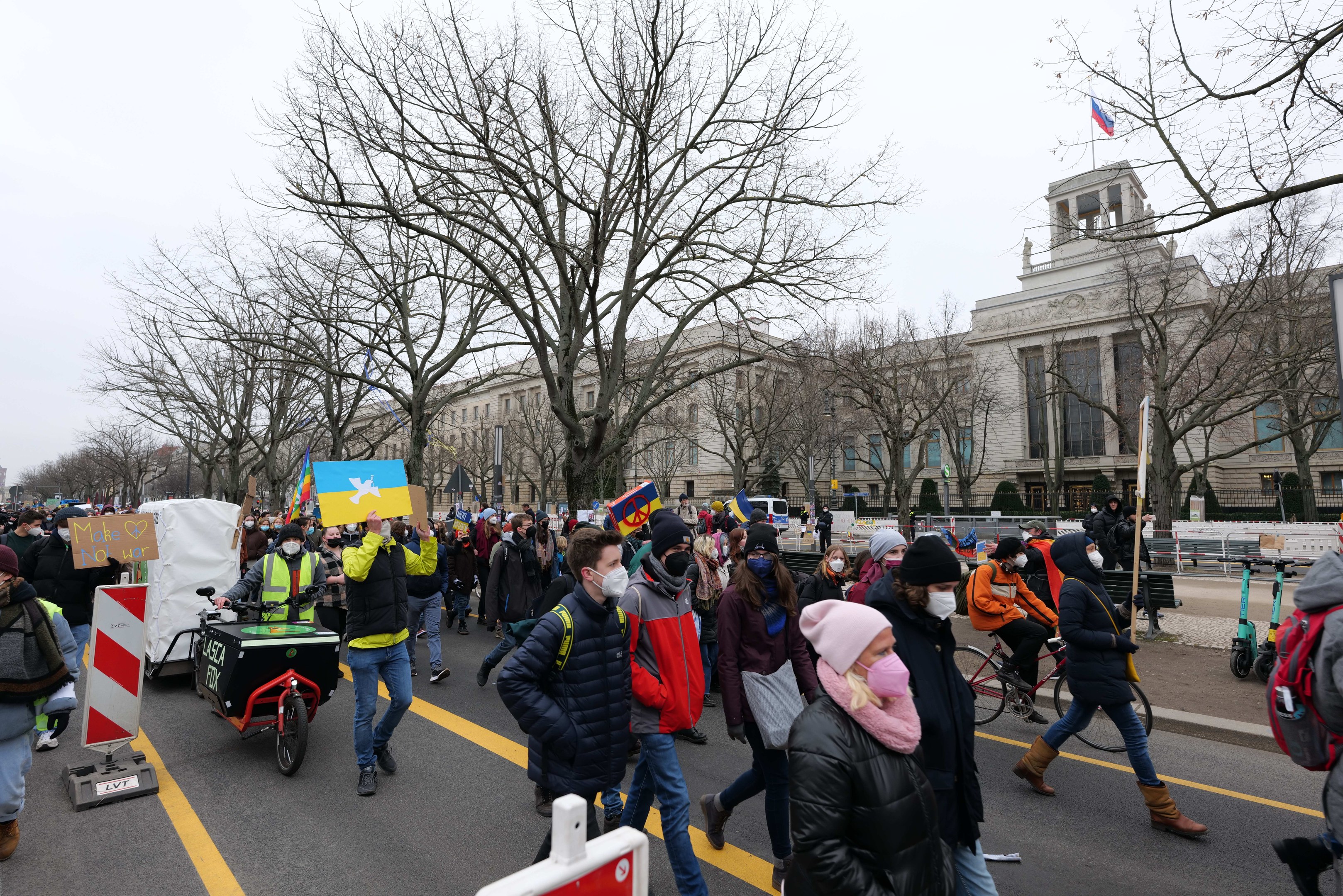 Eine große Gruppe von Menschen marschiert auf einer Straße in Washington, D.C. und hält Schilder, fährt mit Fahrrädern, mit Bäumen und einem klaren blauen Himmel im Hintergrund.
