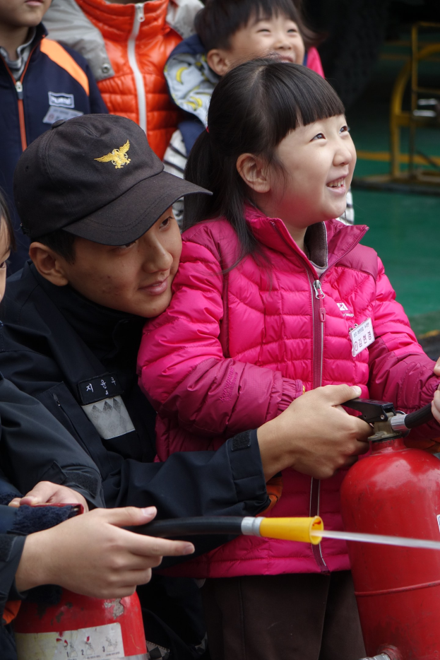 Kinder in einer Schulumgebung umringen einen roten Feuerhydranten, einer hält ein Rohr.