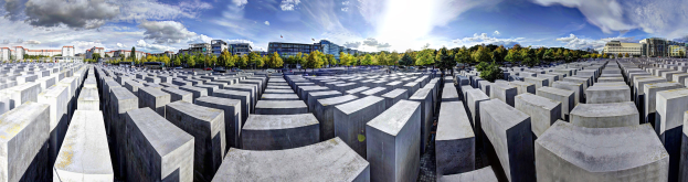 Luftbild des Holocaust-Mahnmals für die ermordeten Juden Europas in Berlin, Deutschland, mit großen Betonsteinen, umgeben von Bäumen und städtischen Gebäuden, mit Fahrzeugen auf der Straße und einem bewölkten Himmel.