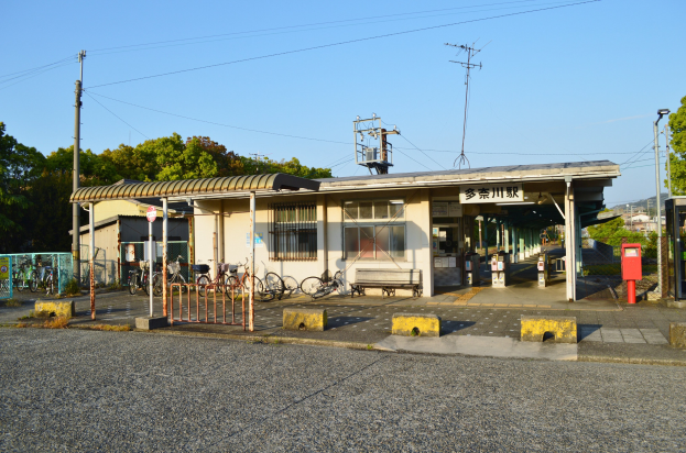 Ein Bahnhof mit Fahrrädern davor, eine Straße unten und Häuser, Bäume, Pfosten, Drähte und einen klaren blauen Himmel im Hintergrund.