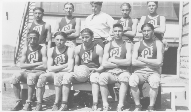 Ein Schwarz-Weiß-Foto einer Basketballmannschaft, die auf einer Bank sitzt, mit einem Mann in der Mitte, der einen Ball hält, und Text unten auf dem Bild.