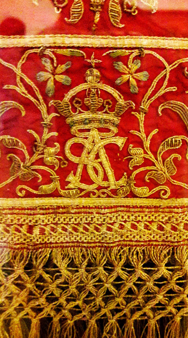Nahaufnahme eines roten und goldenen Tuchs mit einer Krone, das mit kunstvoller Goldstickerei verziert ist.