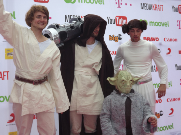 Gruppe von Menschen in Star-Wars-Kostümen auf einem roten Teppich mit einem Banner im Hintergrund posend.
