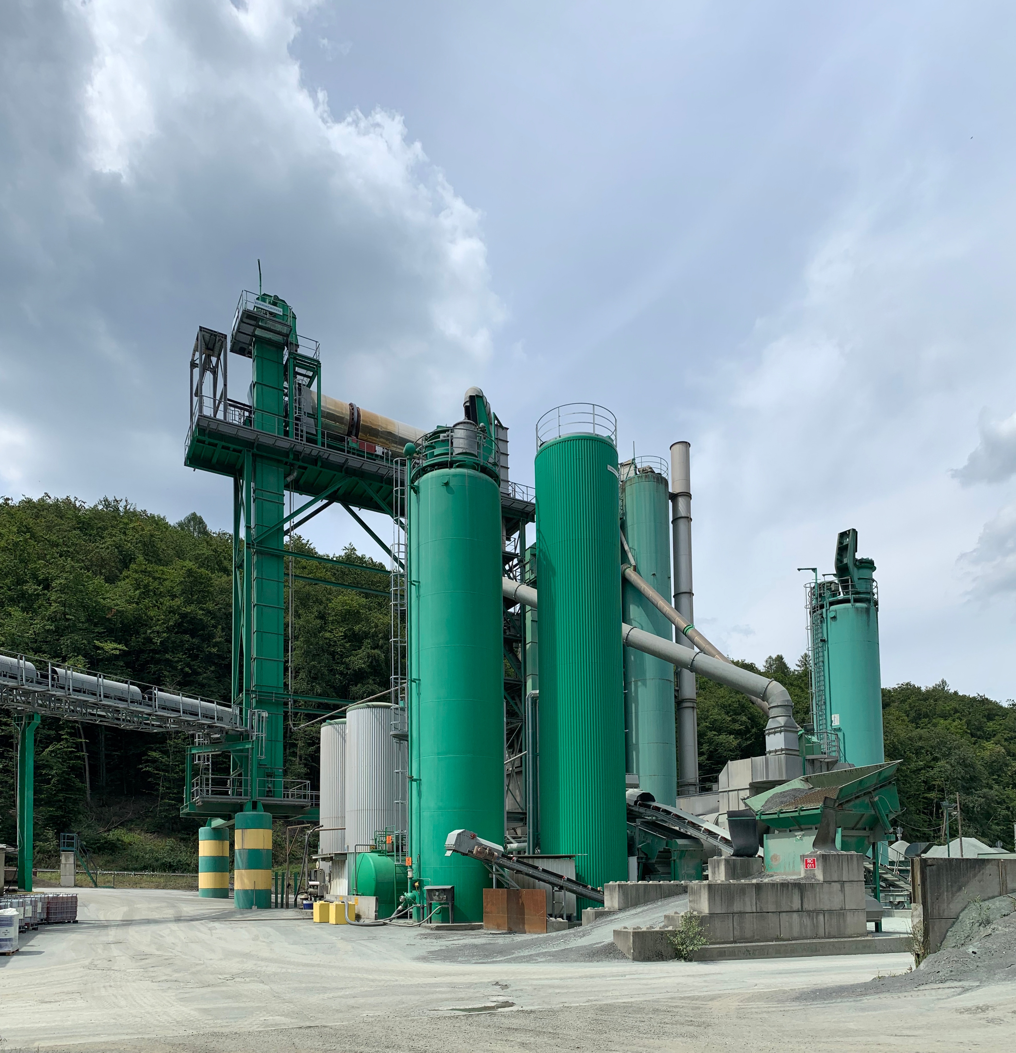 Eine große Industrieanlage für die Pyrolyse von Altreifen mit zahlreichen grünen Tanks, Maschinen und Polen vor einem Hintergrund aus Bäumen und einer bewölkten Himmel