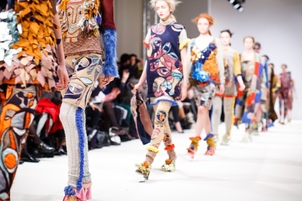Eine Gruppe Von Frauen, Die Eine Laufsteg In London Fashion Week Mit Einem Publikum Im Hintergrund Unter Helleren Lichtern Gehen.