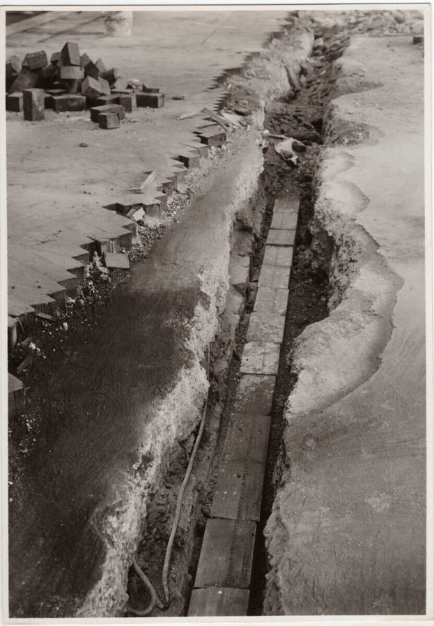 Schwarzes und weiße Foto einer gebrochenen Straße mit verstreuten Ziegeln auf der linken Seite.