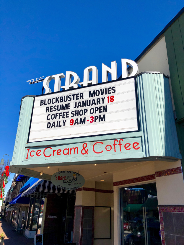 Der Strand-Blockbuster-Kino startet am 18. Januar. Kaffee-Shop-Gebäude mit einem Namensschild, einem Straßenschild, einer Gruppe von Bäumen, einigen Topfpflanzen und einem bewölkten Himmel.