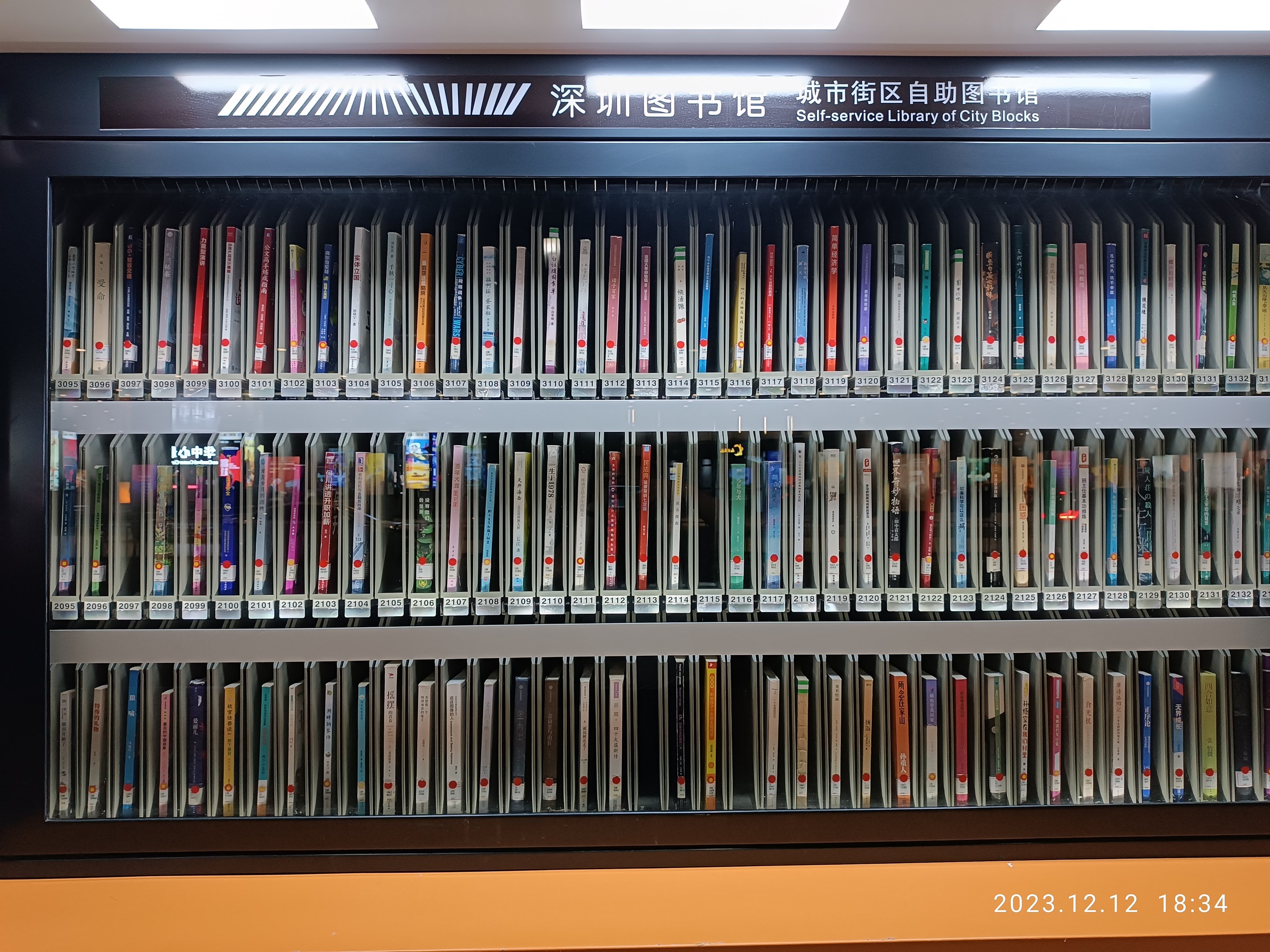 Eine gut beleuchtete Bibliothek mit hohen Bücherregalen voller Bücher, mit einer Tafel mit Text und einem Wasserzeichen unten.