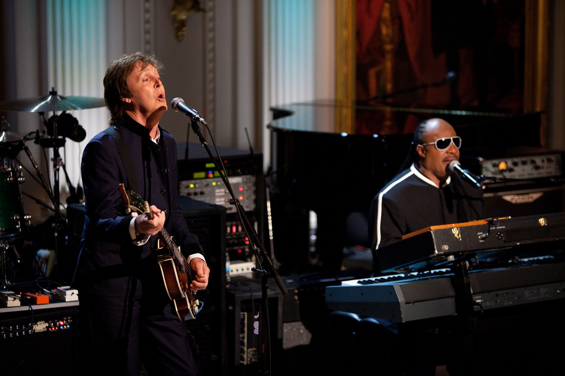 Paul McCartney und Stevie Wonder performen auf der Bühne bei den Grammys, wobei McCartney Gitarre spielt und singt und Wonder eine Brille trägt, während er am Piano spielt.