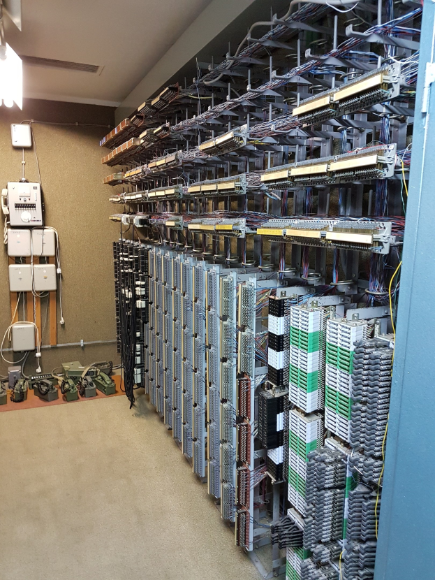 Großer Raum mit zahlreichen Kabeln und elektronischen Geräten auf dem Boden, darunter Server und Kabel, die auf ein Rechenzentrum mit einer Wand auf der linken Seite hinweisen.