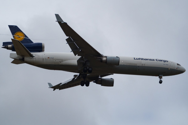 Ein Lufthansa Cargo Boeing 777-300ER im Flug, mit ausgebreiteten Flügeln und laufenden Triebwerken, mit sichtbarem Text auf dem Rumpf gegen einen bewölkten Himmel.