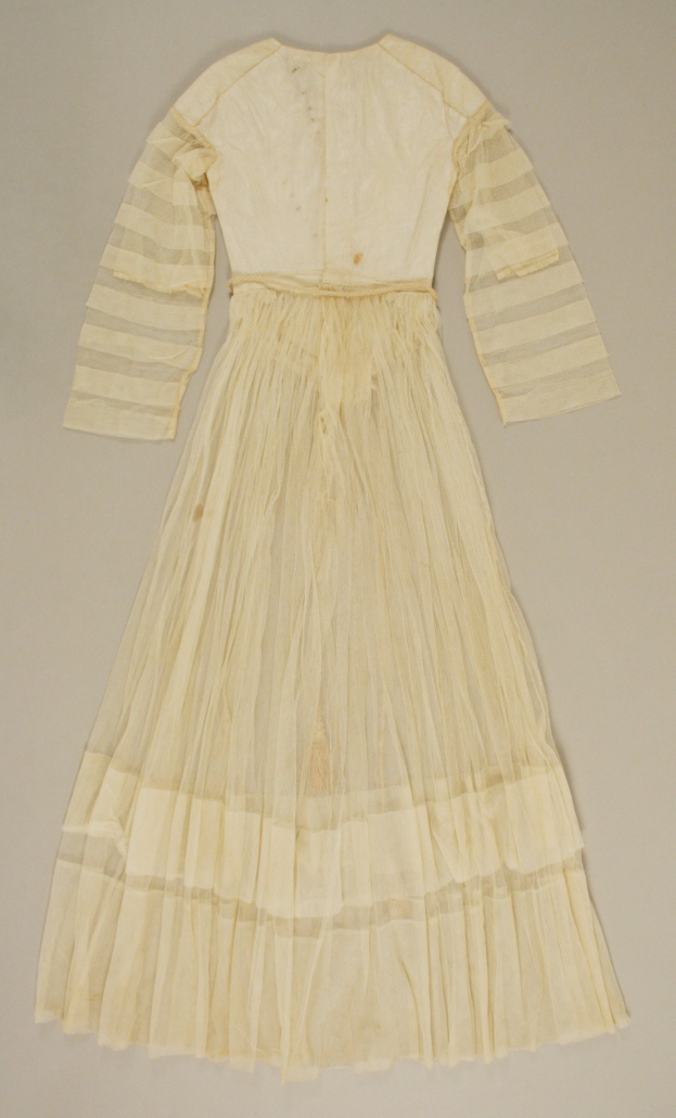 Ein weißes, langärmeliges Kleid mit einer gerüschten, weiten und glänzenden Stoffbahn auf einem weißen Hintergrund.