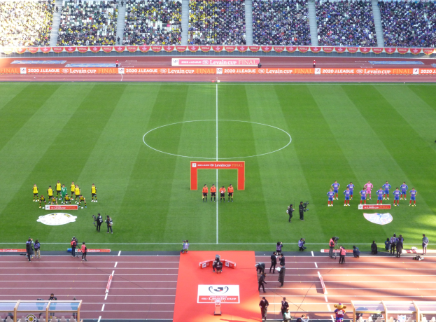 Eine Gruppe von Menschen steht auf einem grünen Fußballfeld in einem Stadion voller Zuschauer, mit Werbetafeln für das Finale des Levin Cups 2020 im Hintergrund.