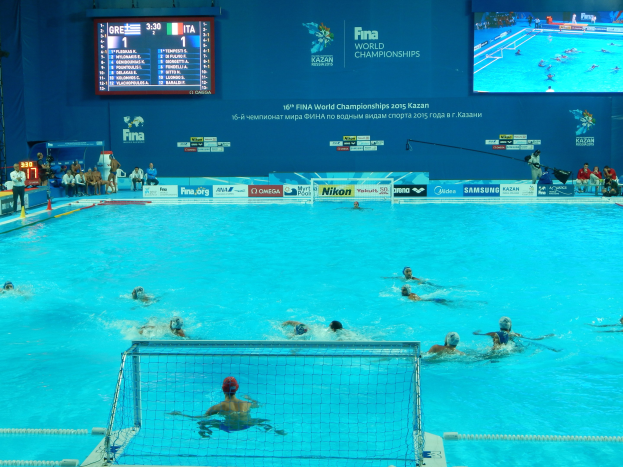 Wasserballspieler bei den 2016 FINA-Weltmeisterschaften in Kazan im Pool gegeneinander antretend, mit Zuschauern auf der linken Seite und einem Scoreboard im Hintergrund.