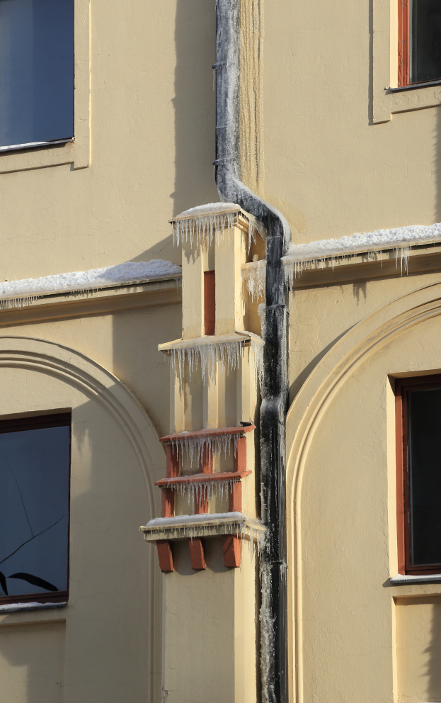 Ein Gebäude mit schneebedeckten Fenstern und Eiszapfen an seiner Seite, das eine sichtbare Rohrleitung zeigt.