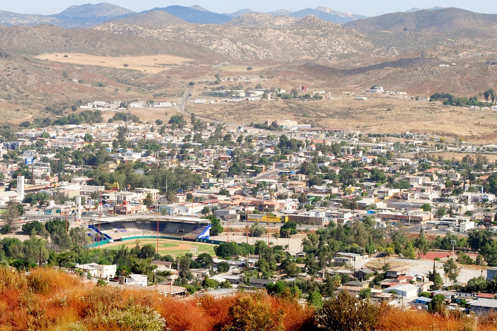 Eine Landschaft mit Häusern, Bäumen, Strommasten, Hügeln und Himmel.