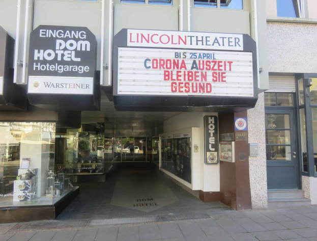 Das Lincoln Theater in Berlin, Deutschland, ein Gebäude mit Glasfenstern und -türen und einer Tafel mit Text darauf, das verschiedene Objekte zeigt, die einen belebten Stadtbild Eindruck vermitteln.
