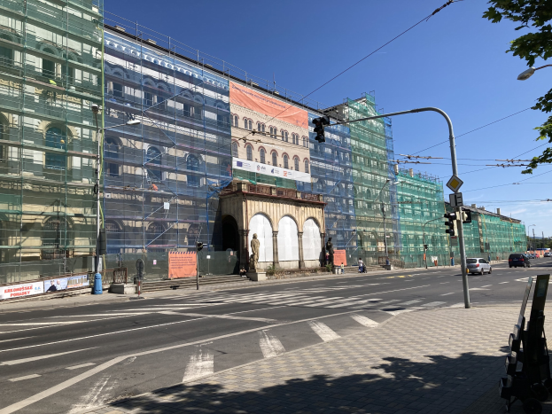 Großer mehrstöckiger Bau im Bau in Berlin mit zahlreichen Fenstern, umgeben von Straßeninfrastruktur, Fahrzeugen, Fußgängern und Bäumen bei einem bewölkten Himmel.