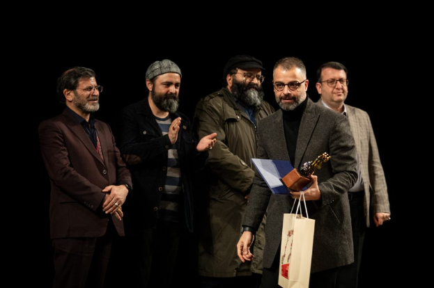 Eine Gruppe von Männern auf einer Bühne bei Nacht, einer hält eine Tasche und eine Trophäe, feiernd die Eröffnung des Berliner Filmfestivals.