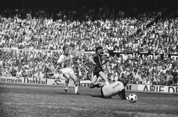 Schwarzes Foto von Männern, die auf einem Feld Fußball spielen, mit Zuschauern im Hintergrund und einem Banner 'Bundesliga 1978-79 Ajax 1-1 Hannover 96'.